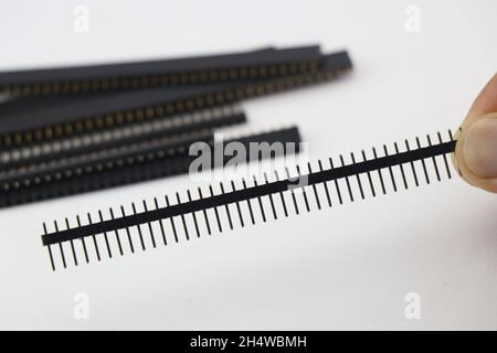 Pin header male connector held in hand with a group of other header pins on the background Stock Photo