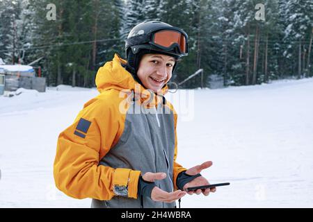 Portrait attractive happy smiling snowboarder with smartphone. A Caucasian guy in a sportswear and a helmet on the ski slope. Snowboarder communicates Stock Photo