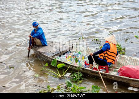 Poor workers are picking up plastic bottles that pollute the environment on the river in Vietnam Stock Photo