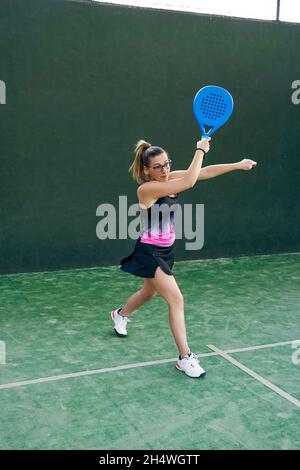 Woman playing paddle tennis, hitting the ball forehand, coming off the wall. Concept of sport Stock Photo