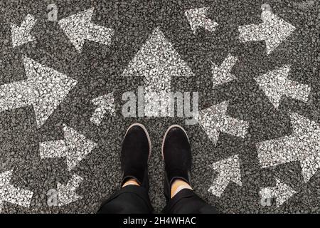 Person standing on road with arrow markings pointing in different directions, decision making concept Stock Photo