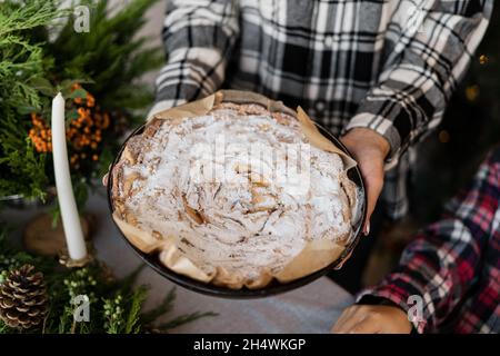 Christmas cake in the form. Female hands hold the shape with an apple pie. Homemade cakes with powdered sugar. Bake for Christmas Stock Photo