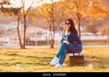International Day of the Blind. A young woman in black sunglasses is sitting on a bench in an autumn park. The concept of loneliness and disability. Stock Photo