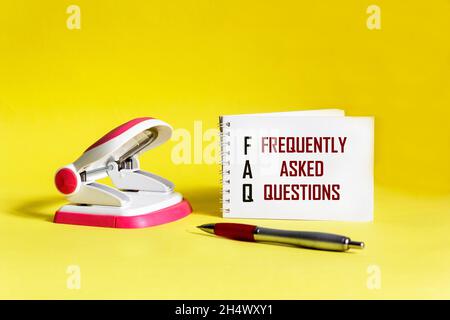 FAQ text, frequently asked questions, on a notepad, on a yellow background with a stapler Stock Photo