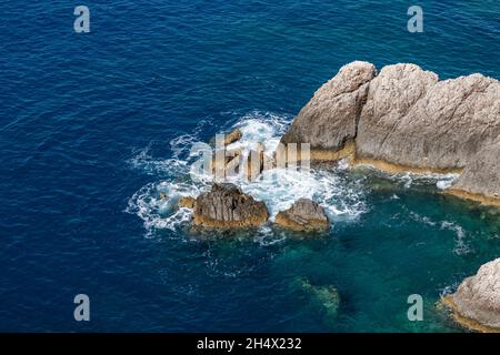 Clear white waves hitting rocks in blue Ionian sea. Summer nature in Lefkada island, Greece. Top aerial view Stock Photo
