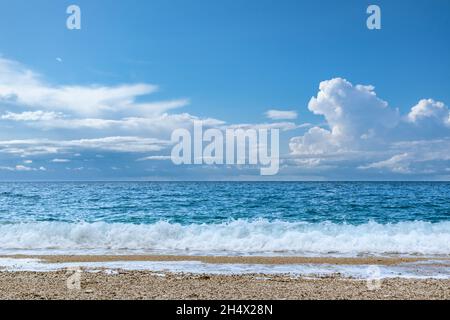 Scenic pebble beach with blue stormy waves and white foam. Epic cloudscape on coast of Lefkada island in Greece. Summer nature vacation travel to Ioni Stock Photo