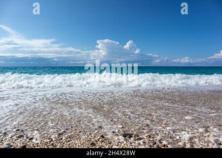 Scenic pebble beach wide view with blue stormy waves and white foam with epic cloudscape on coast of Lefkada island in Greece. Summer vacation to Ioni Stock Photo