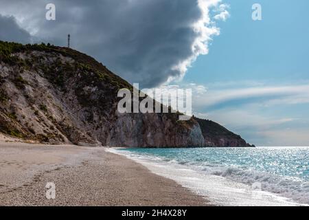 Epic stormy clouds on warm summer Mylos pebble beach. Idyllic coast with high cliffs of Lefkada island in Greece. Summer travel to turquoise Ionian Se Stock Photo