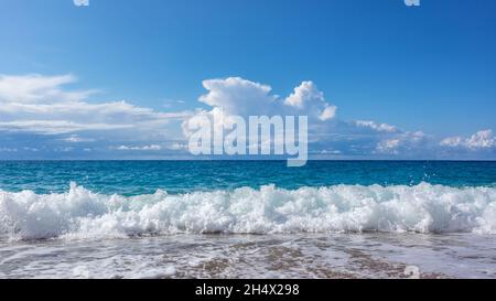 Scenic sunny pebble beach with blue stormy waves and white foam. Epic cloudscape on shoreline of Lefkada island in Greece. Summer nature vacation trav Stock Photo
