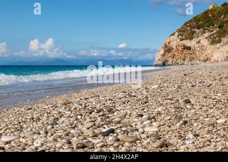 White pebble stones close-up on Mylos beach with azure waves and white foam. Coast of Lefkada island in Greece. Summer travel to Ionian Sea Stock Photo
