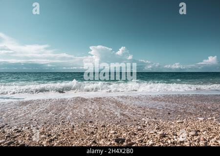 Scenic pebble beach with turquoise stormy waves and white foam with epic cloudscape on coast of Lefkada island in Greece. Nature vacation travel to Io Stock Photo