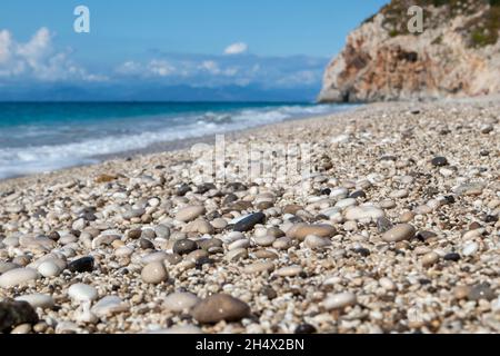 Mylos beach white wet shiny pebble stones close-up with azure sea, stormy waves, epic clouds and rocky cliff on coast of Lefkada island in Greece, Ion Stock Photo