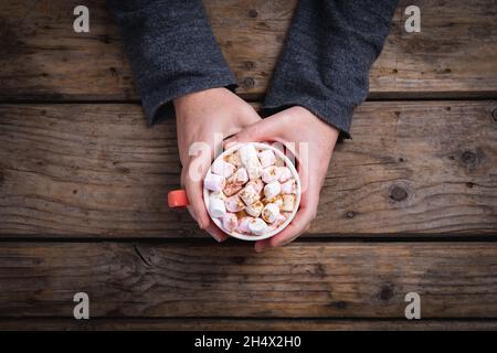 Overhead view of female hands holding mug of hot chocolate drink filled with marshmallows at table Stock Photo
