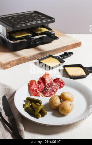 Traditional dish of raclette served with baby new potatoes, charcuterie and pickles. Stock Photo