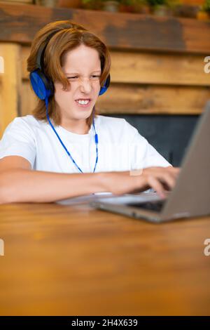 A teenager during a computer game - he sits in front of a laptop computer and screams. Emotional release during computer games. Gaming addiction conce Stock Photo