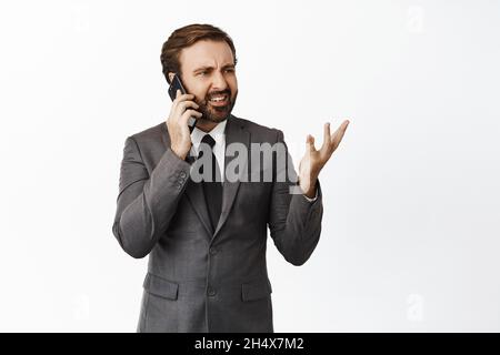 Angry corporate man arguing on cellphone, having intense phone call, standing over white background Stock Photo