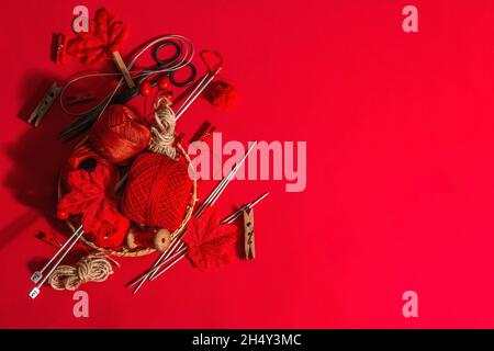 Festive handmade concept. Threads, knitting needles, vintage scissors, autumn decor. Monochrome objects in red colors on a rough background, top view Stock Photo