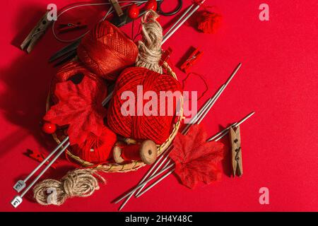 Festive handmade concept. Threads, knitting needles, vintage scissors, autumn decor. Monochrome objects in red colors on a rough background, top view Stock Photo