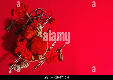 Festive handmade concept. Threads, knitting needles, vintage scissors, autumn decor. Monochrome objects in red colors on a rough background, top view Stock Photo