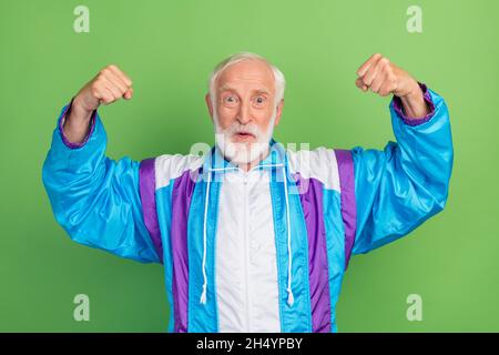 Photo of impressed funny mature guy dressed blue sport smiling rising fists isolated green color background. Stock Photo