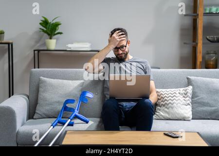 Injured Man With Broken Leg And Crutches Using Laptop Stock Photo