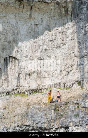 Cliff face, view in summer of two young people preparing to climb Malham Cove, a sheer 260ft high cliff in the North Yorkshire Dales, England, UK Stock Photo
