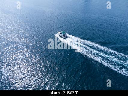 A boat in the sea races on the water, leaving a trail of foam on the water Stock Photo