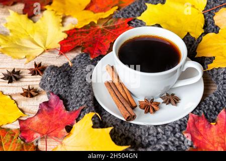 Cozy autumn morning with cup of coffee with cinnamon, star anise, cozy sweater and autumn leaves on wooden background. Hot coffee with spices on the o Stock Photo