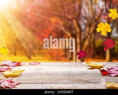 Wooden table top on blur autumn background. Autumn golden abstract background with bokeh light and colorful leaves. Stock Photo