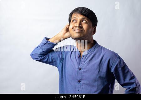 A young Indian male in blue dress scratching head and thinking on white background Stock Photo