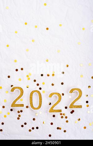 New Year Candles in shape of numbers 2022 on white wrapping paper with gold confetti flat lay view