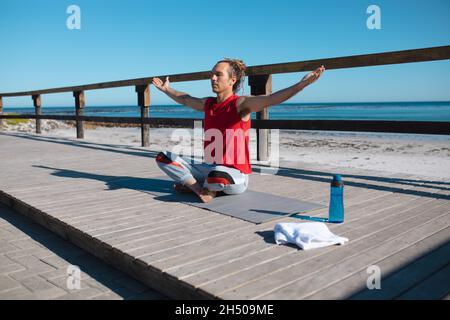 Man sitting cross-legged and arms outstretched meditating while practicing yoga on floorboard Stock Photo