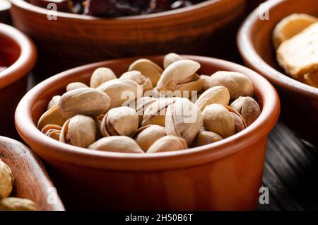 Pistachio nuts in clay bowl on kitchen wooden table food background Stock Photo