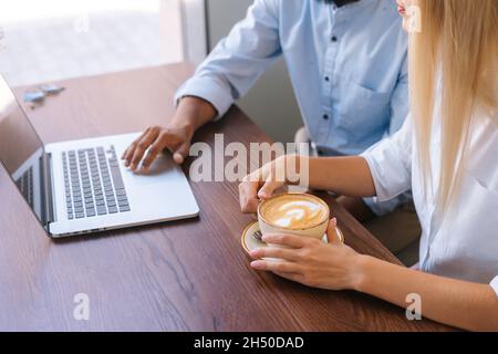 Close-up top view hands of unrecognizable business man and woman working with laptop sitting at table in cafe. Stock Photo