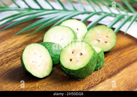 Fresh green feijoa (pineapple guava) fruit slices on brown wooden background in the kitchen. Stock Photo
