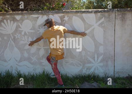 Rear view of male artist touching abstract mural painting on wall while walking on grass Stock Photo