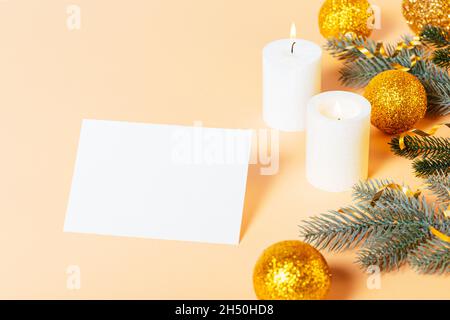 Christmas and New Year composition with blank greeting card template next to candles, golden Christmas balls and fir branches on beige background Stock Photo
