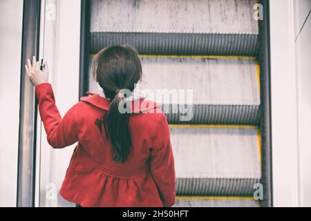 Woman commuter going to work walking up escalator stairs commuting in train station or airport. Stock Photo