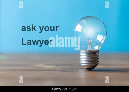 On the blue wall the words are written: ask yout lawyer. Next to the writing, an ancient light bulb with glowing light stands freely and upright on a Stock Photo