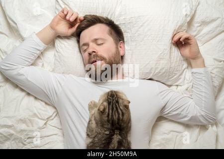Man in white pajamas is asleep, and his adorable cat lies on his chest. Top view.  Stock Photo