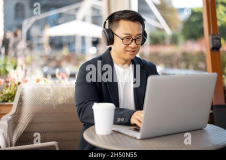 Businessman in earphones working on laptop in cafe Stock Photo