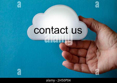 Hand holds a white cloud symbol against a blue background. The text is written on the cloud: contact us Stock Photo