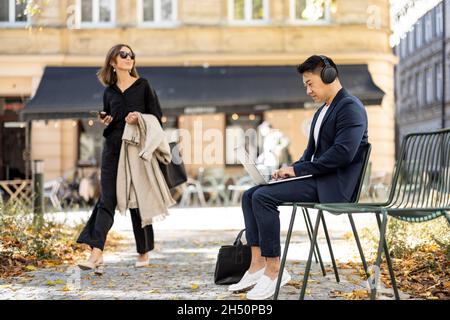 Businessman work on laptop and woman go in city Stock Photo