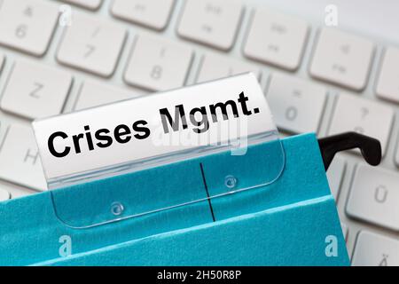 The words  crises Management can be seen on the label of a blue hanging folder. The hanging folder is on a computer keyboard. Stock Photo