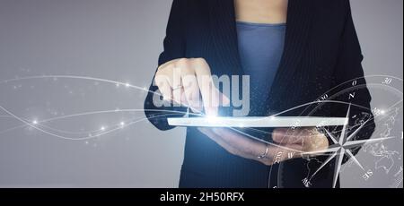 Business navigate recovery. White tablet in businesswoman hand with digital hologram Compass sign on grey background. The compass navigate for busines Stock Photo