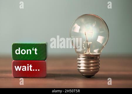don't wait are the word written on a red and a green toy block. Next to the tow blocks, an ancient light bulb with glowing light stands freely and upr Stock Photo