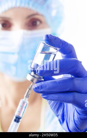 Caucasian female doctor in protective gloves and mask fill syringe with medicine for injection