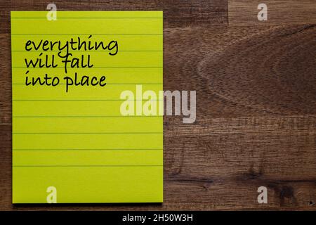 yellow sticker with lines on a dark wooden background with the handwriting of the wisdom of life: everythin will fall into place Stock Photo