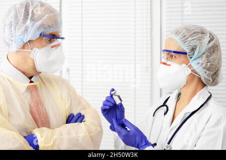 Male and female health care workers in masks caps and gloves having discuss indoors Stock Photo