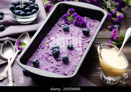 Blackberry icecream in metal tray served with flower buds and blackberries on kitchen table Stock Photo
